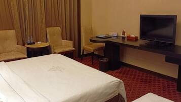 A hotel room with a bed, two armchairs, a desk with a television, and a small table with a bottle and a glass.