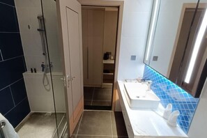 A bathroom with a glass shower enclosure, a white sink, and a blue-tiled accent wall. - Master Hotel (Huidong)
