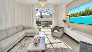 Ein modernes Wohnzimmer mit großem Fernseher, einer Couch, einem Couchtisch und Blick auf Pool und Strand.