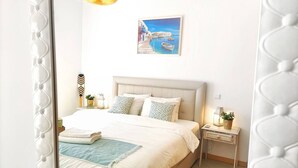 A bedroom with a bed, bedside tables, a nightstand, a hanging light, and a wall-mounted painting.