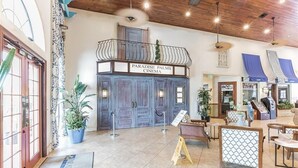 A lobby with a cinema named 'Paradise Palms Cinema', featuring a wooden balcony, potted plants, and a reception area with a counter and chairs.
