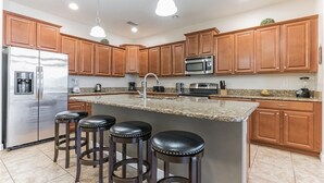 A modern kitchen with wooden cabinets, stainless steel appliances, a granite countertop, and three bar stools.