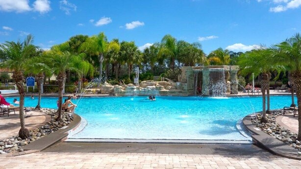 A large outdoor swimming pool with palm trees and a waterfall feature.