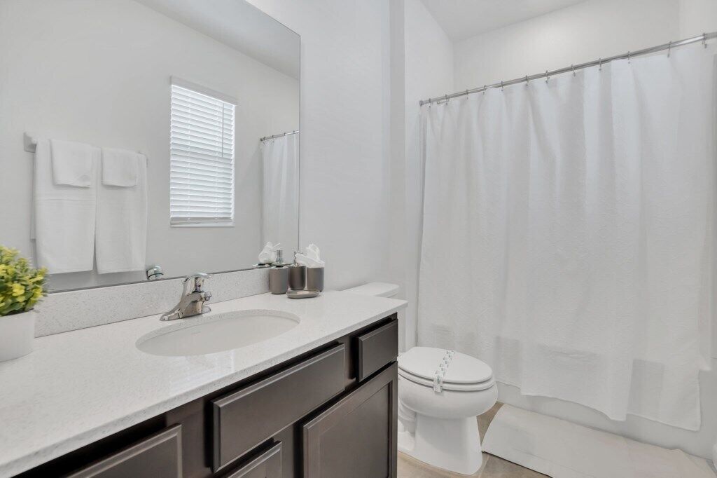 Un baño moderno con un lavamanos, espejo y retrete blancos.