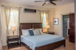 A bedroom with a bed, two bedside tables with lamps, a ceiling fan, an air conditioning unit, and a door leading to a shower area. - Family time, 5 minute walk from main walkway to restaurants and beach! (Vieques)