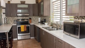 A modern kitchen with dark wood cabinets, stainless steel appliances, a tiled backsplash, and a large window providing natural light. - Family time, 5 minute walk from main walkway to restaurants and beach! (Vieques)