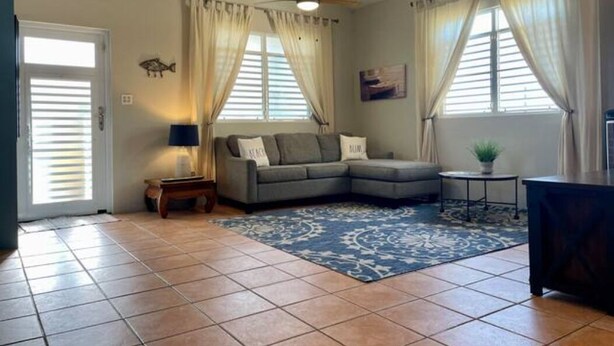 A living room with a sectional sofa, a blue patterned rug, a ceiling fan, and a small side table with a lamp. - Family time, 5 minute walk from main walkway to restaurants and beach! (Vieques)