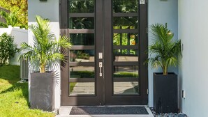 Une entrée moderne avec une porte double de couleur sombre, deux plantes en pot et un chemin en béton menant à la porte.