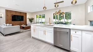 Une cuisine moderne avec des meubles blancs, des appareils en acier inoxydable et des luminaires suspendus.