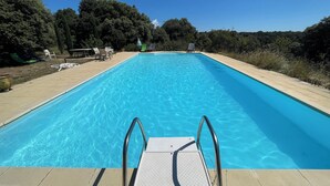 En rektangulær swimmingpool med krystalklart, blå vand, omgivet af en flisbelagt terrasse.