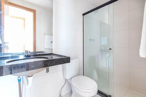 A modern bathroom with a glass shower enclosure, a white toilet, and a granite countertop sink.