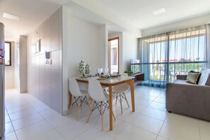Uma sala de estar moderna com área de jantar, janelas grandes e um sofá cinza.