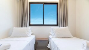 Una habitación pequeña y limpia con dos camas individuales, una ventana con cortinas y una mesita de noche de madera.