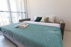 Uma cama bem arrumada com um edredom verde, almofadas brancas e uma toalha dobrada.