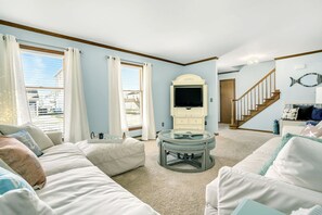 Ein Wohnzimmer mit großem Fenster, einem Flachbildfernseher, einem runden Glastisch und einer Treppe, die zu einer weiteren Ebene führt.