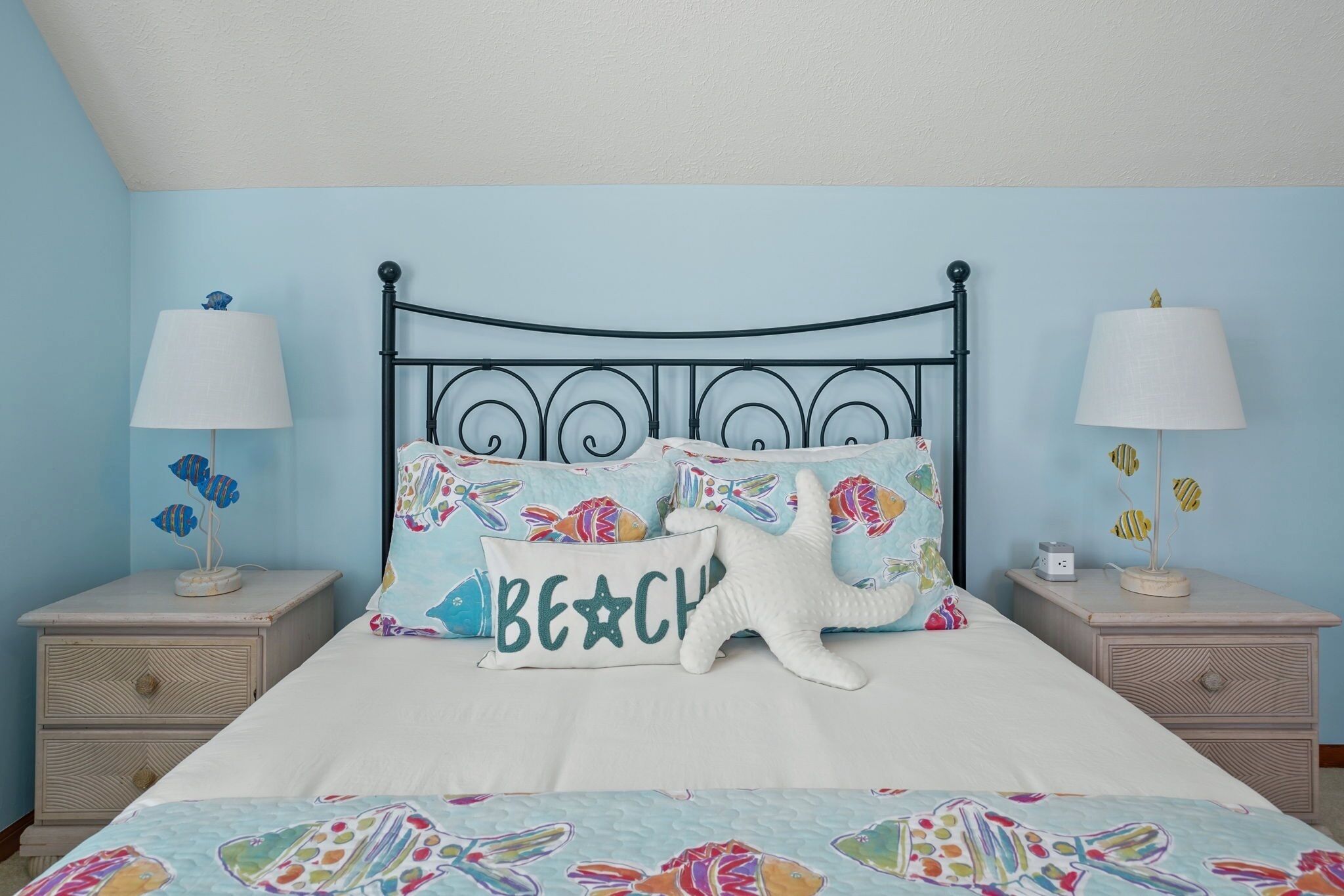 A bedroom with a bed, two nightstands, and a wall with a light blue color.