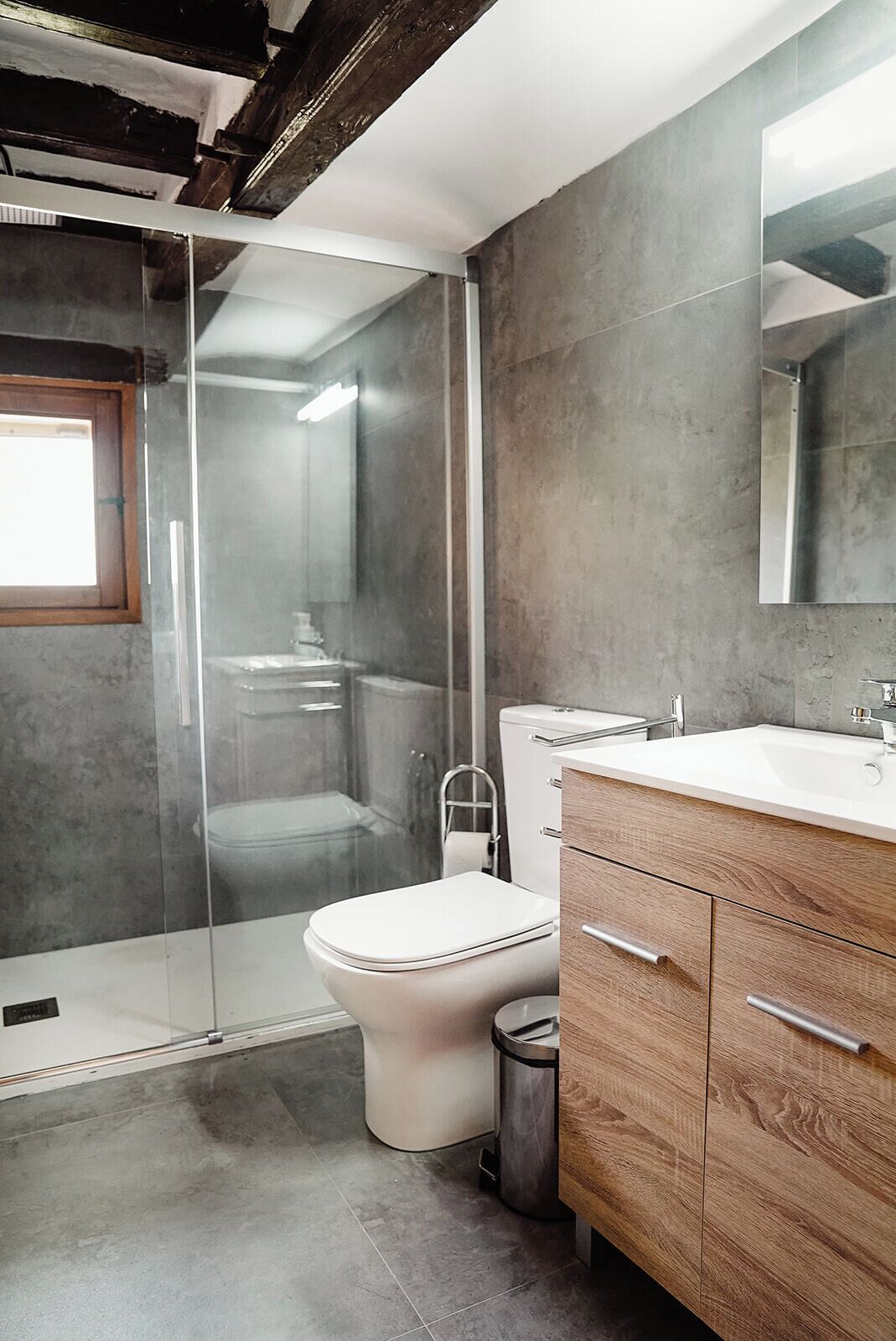 Un baño moderno con cabina de ducha de vidrio, inodoro blanco y tocador de madera con espejo.