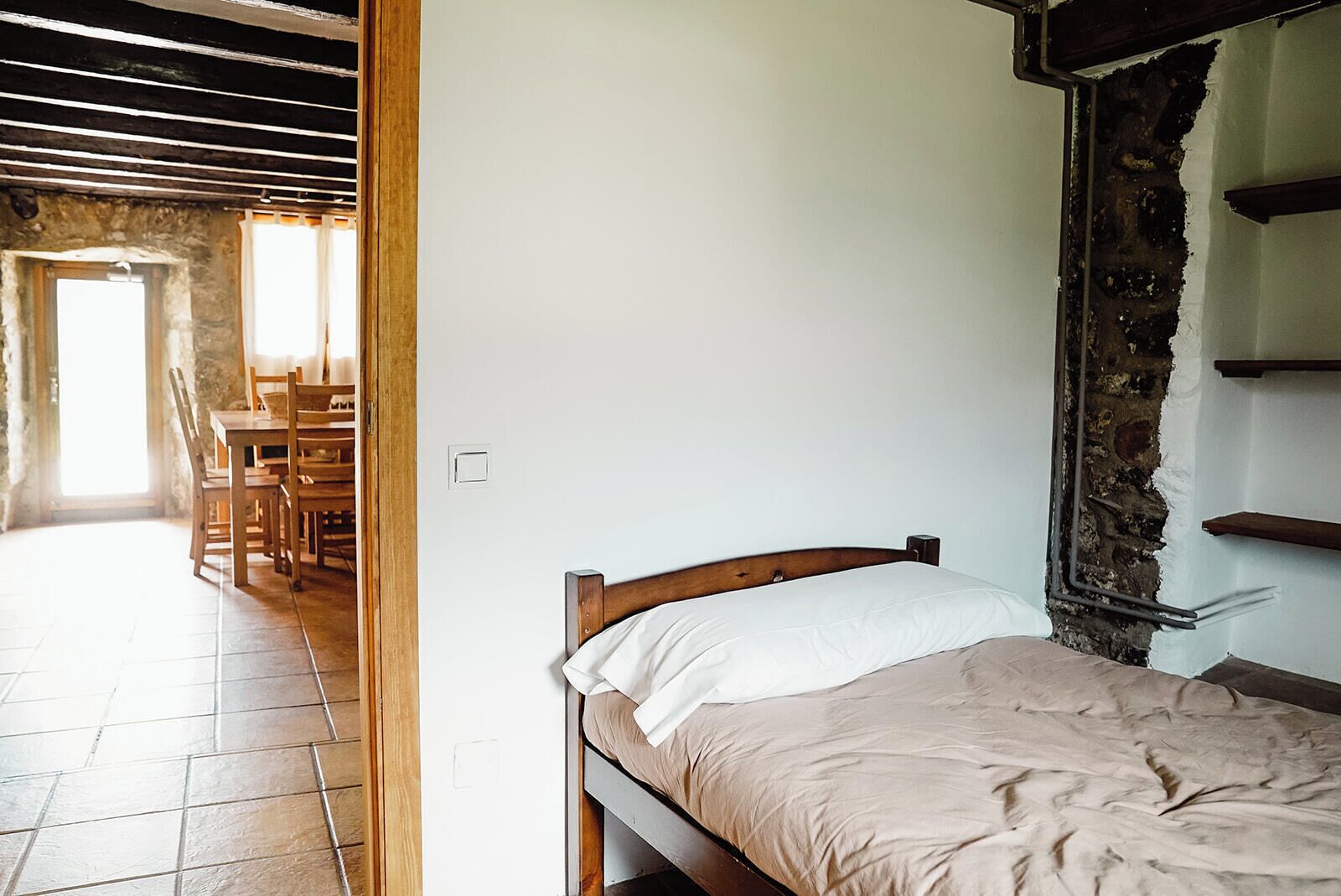 A bedroom with a wooden bed, a white wall, and a stone wall.