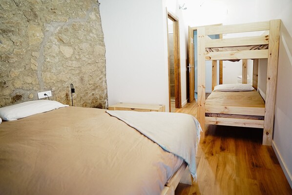 A room with a single bed, a wooden bunk bed, stone walls, and a white door. - Cases Altes de Posada (Navès)