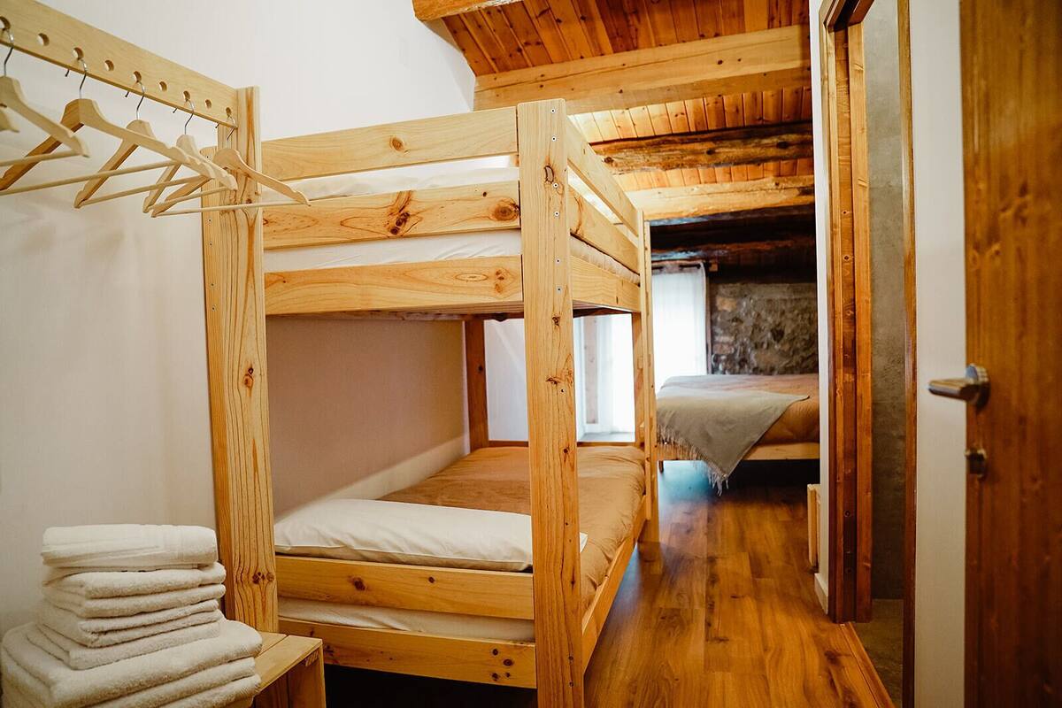 A wooden bunk bed room with a wooden wardrobe and a stack of towels.