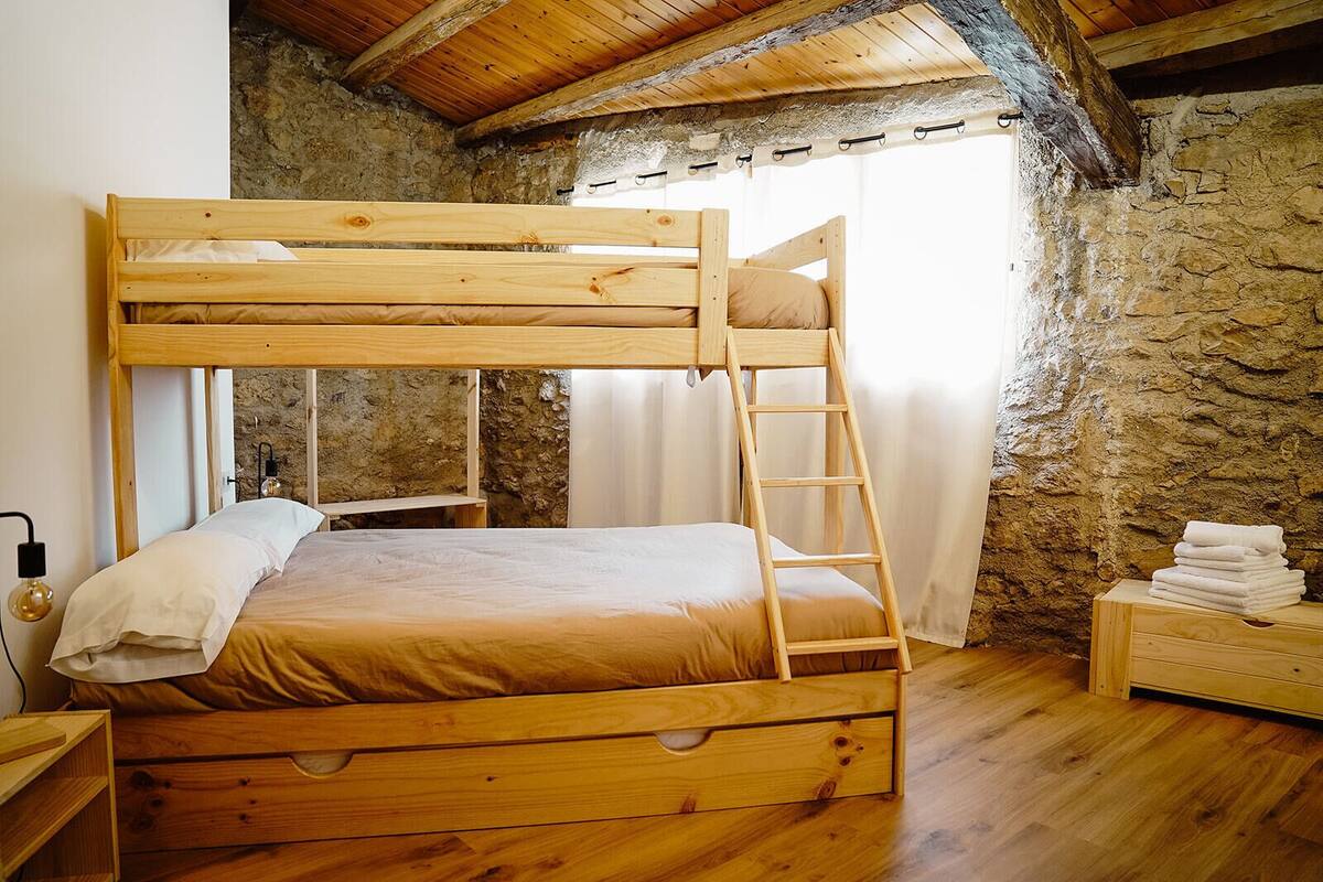 A wooden bunk bed with a ladder, a bedside table, and a stack of towels.