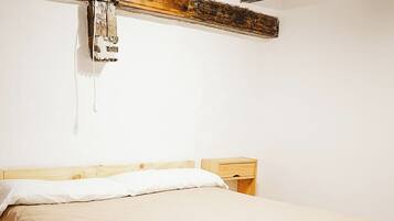 A single bed with a wooden frame and a beige mattress in a room with exposed wooden beams and tiled flooring.