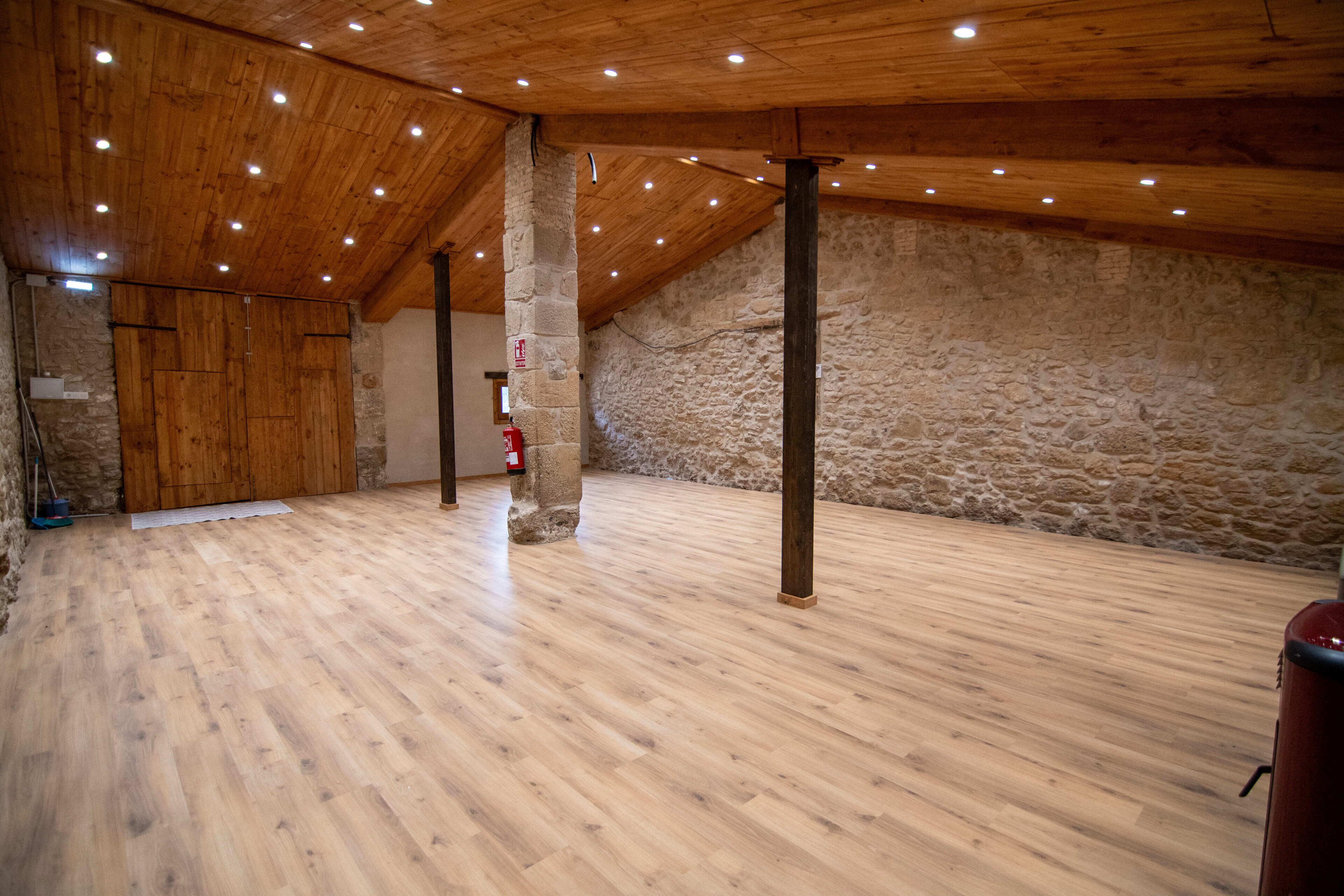 Een ruime zolderkamer met houten vloeren, stenen muren en een schuine balken plafond met ingebouwde verlichting.