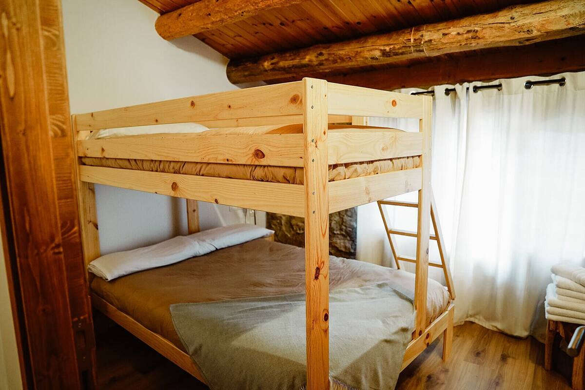 A wooden bunk bed with a ladder, a pillow, and a blanket in a room with wooden walls and a sloped ceiling.