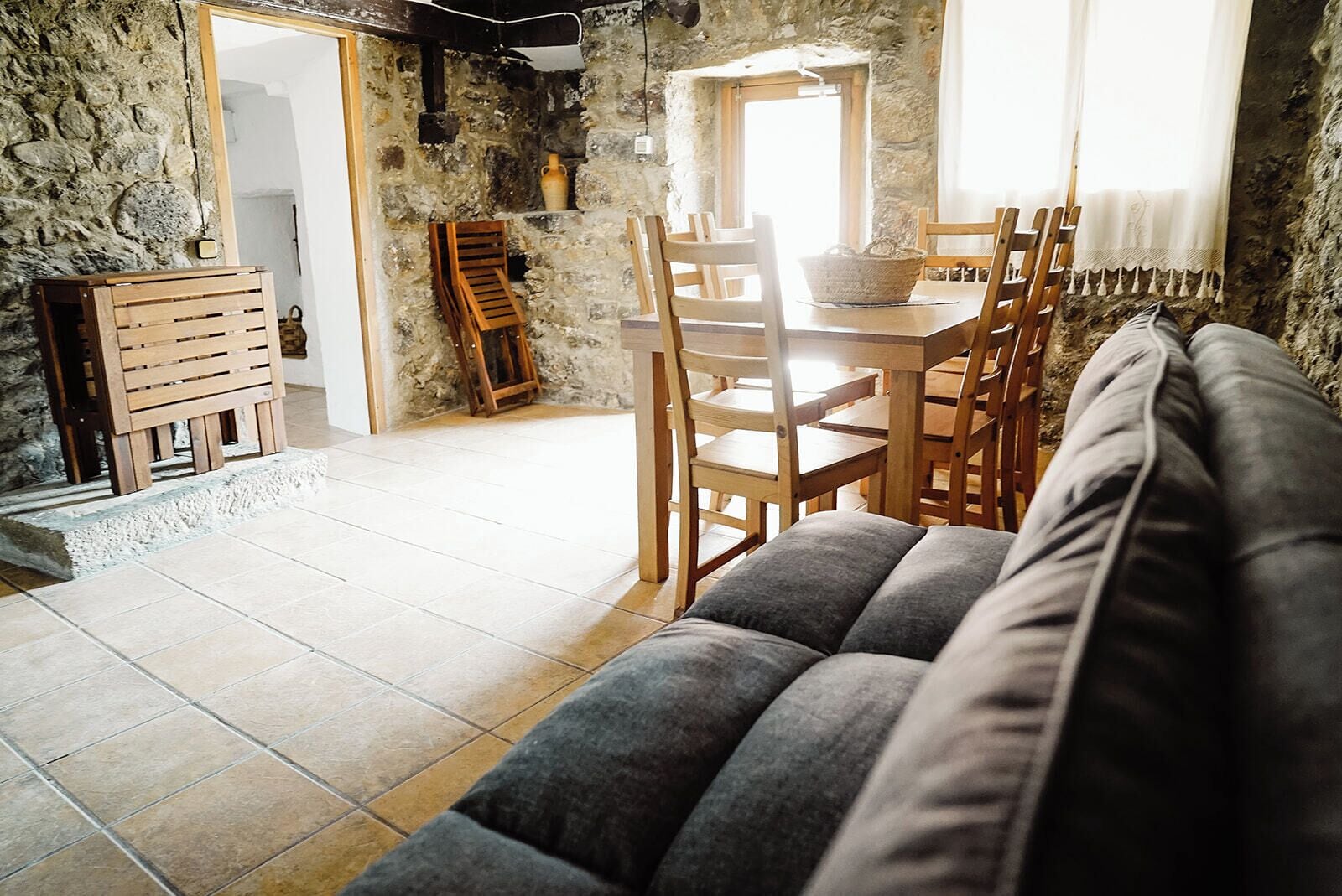 Una sala acogedora con un sofá, una mesa de comedor de madera, sillas y una pared de piedra.
