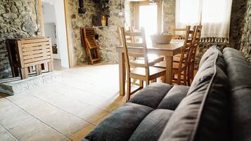Una sala acogedora con un sofá, una mesa de comedor de madera, sillas y una pared de piedra.