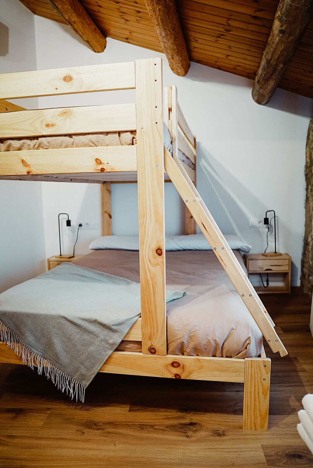 Een houten stapelbed met een ladder, nachtkastje en een stopcontact.