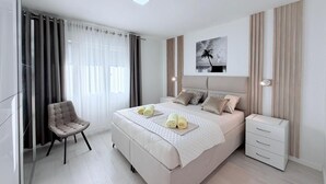 A modern bedroom with a bed, bedside tables, a chair, and a painting on the wall. - Palma Apartments (Kotor)