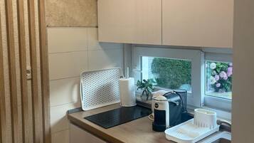 Une cuisine compacte équipée d’un évier, d’une bouilloire et d’un grille-pain. Une fenêtre offre une vue sur la verdure environnante.