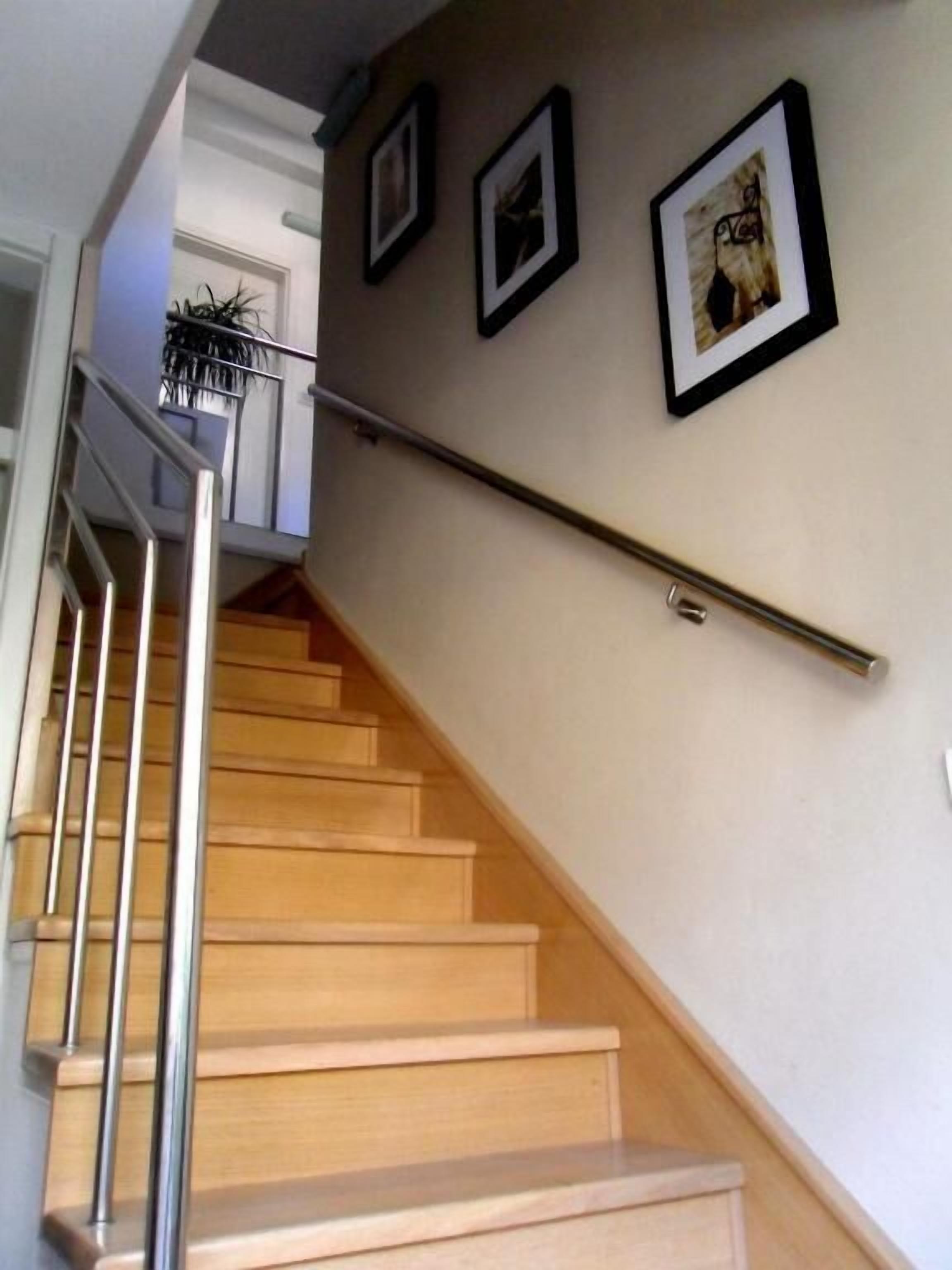 A wooden staircase with a metal handrail, leading to a landing with a potted plant.