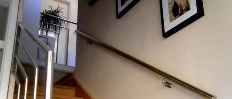 A wooden staircase with a metal handrail, leading to a landing with a potted plant.