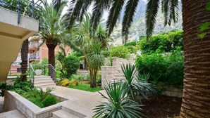 A lush courtyard with palm trees, a stone staircase, and a view of a mountainous landscape. - Palma Apartments (Kotor)