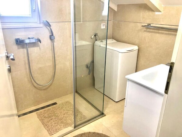 A compact bathroom with a glass shower enclosure, a built-in washing machine, and a white sink.