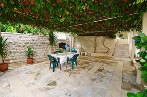 An outdoor patio with a stone floor, a table with chairs, potted plants, and a stone wall. - Palma Apartments (Kotor)