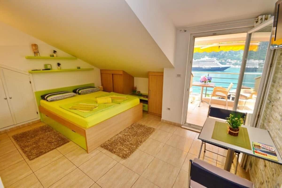 A bedroom with a bed, a small table, and a balcony with a view of the sea.