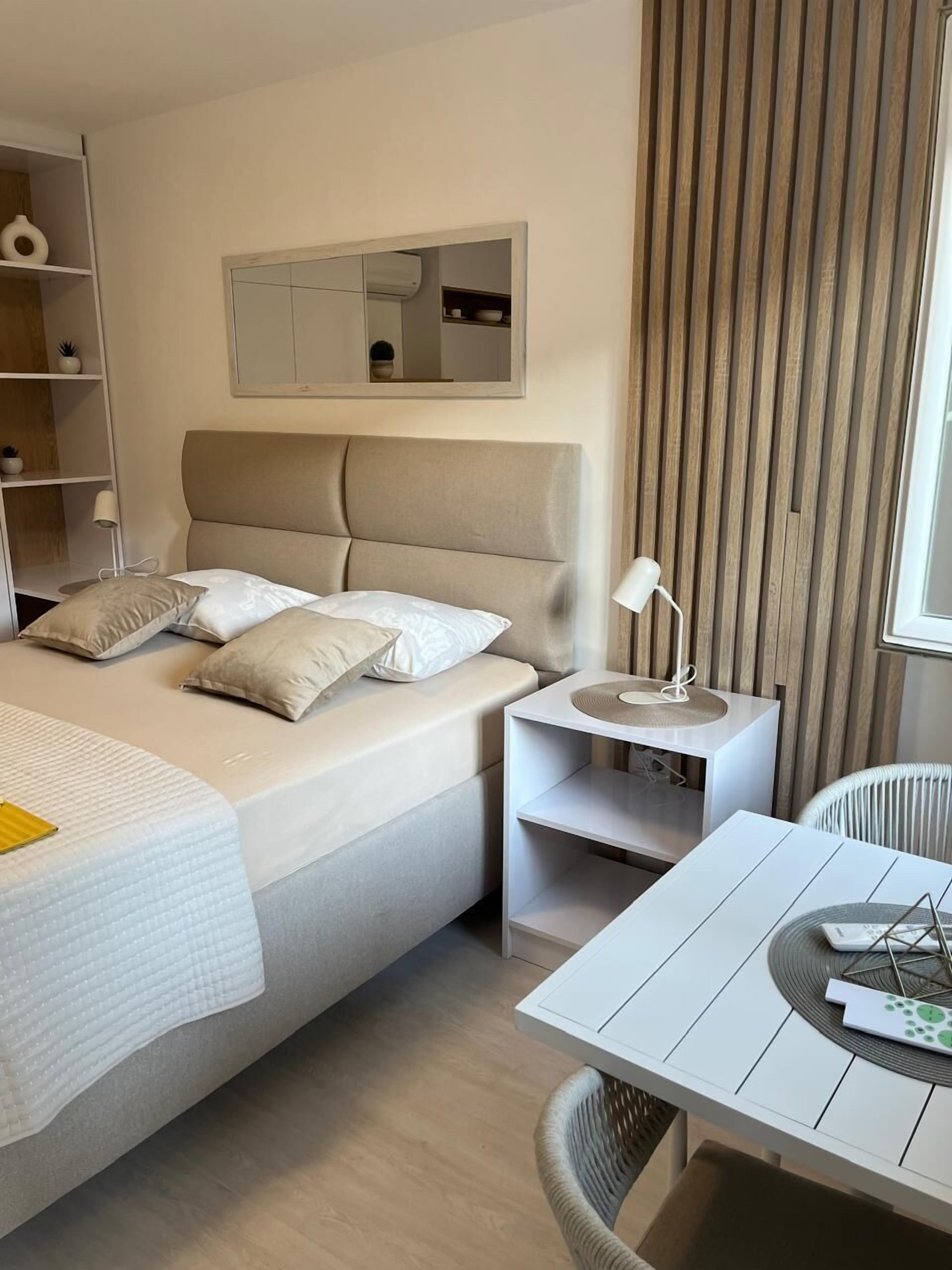 A modern hotel room with a large bed, bedside tables, a small table with a lamp, and a chair.