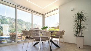 A modern room with large windows, a dining table with chairs, and a potted plant. - Palma Apartments (Kotor)