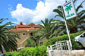 A residential building with a red-tiled roof, surrounded by lush greenery and palm trees. - Palma Apartments (Kotor)