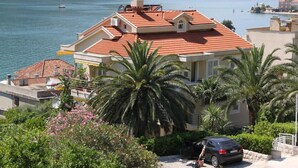 A coastal building with a red-tiled roof, palm trees, and a view of the sea. - Palma Apartments (Kotor)