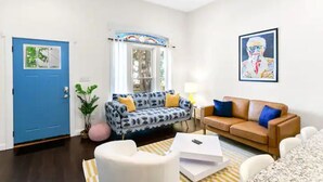 Un salon avec une porte bleue, un canapé à motifs, un canapé marron, un fauteuil blanc et une table basse.