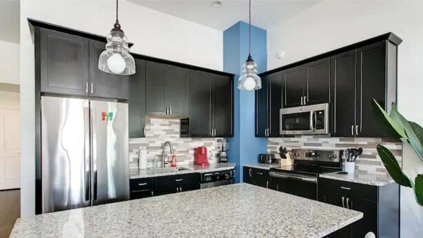 Une cuisine moderne avec des meubles de couleur sombre, un plan de travail en granit, des appareils électroménagers en acier inoxydable et des luminaires suspendus.