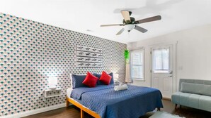 Une chambre à coucher avec un lit, un ventilateur de plafond, une fenêtre et une porte.