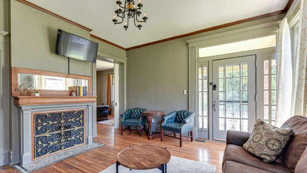 A spacious living room with a fireplace, leather chairs, a round coffee table, and a television mounted on the wall. - Experience History in Style in an 8BR/8BA Private Guesthouse! (Columbus)