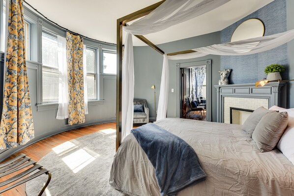 A bedroom with a four-poster bed, a fireplace, and a view of the outdoors.