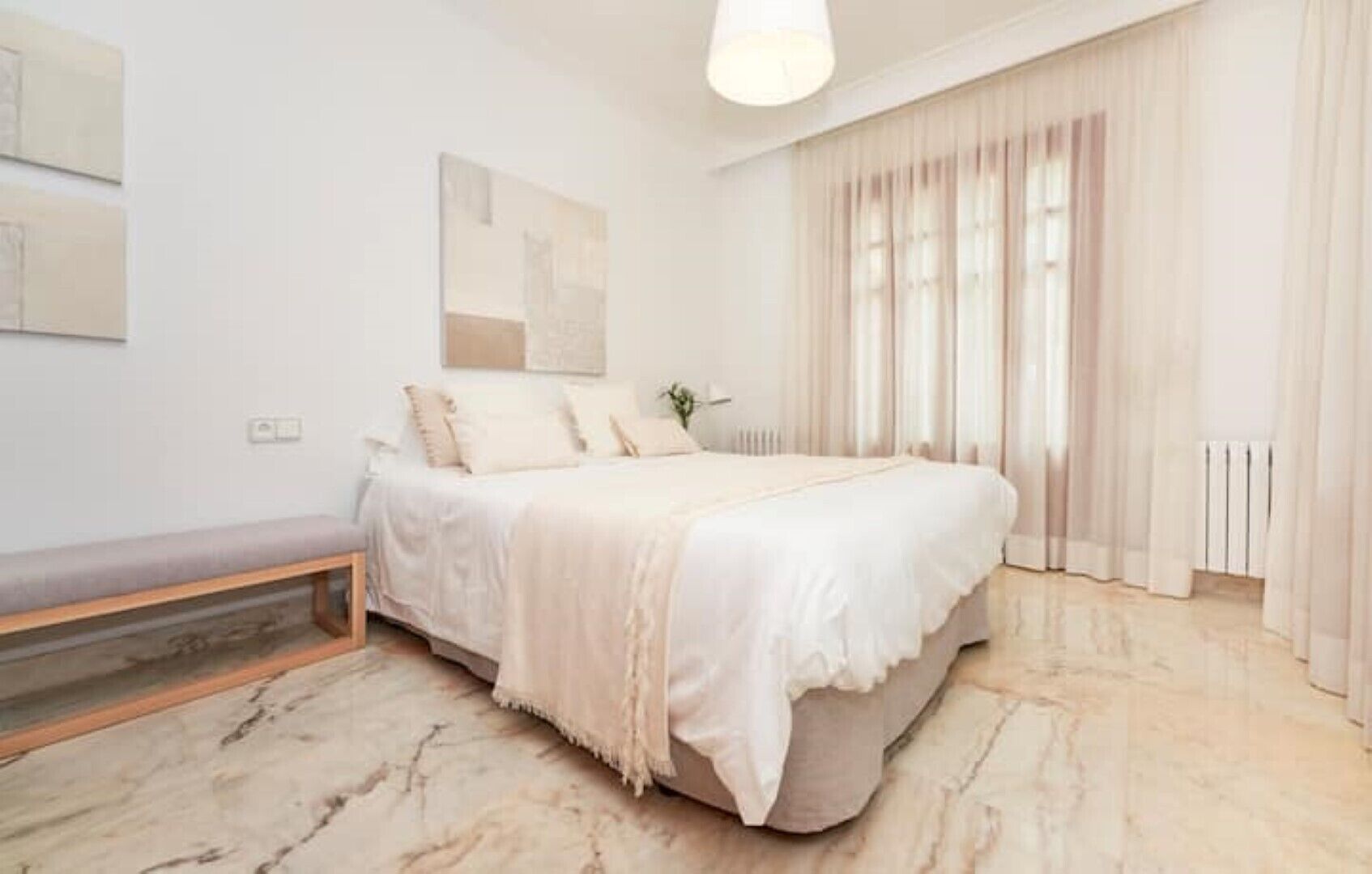 Un dormitorio con una cama, un banco, un radiador y una ventana con cortinas.