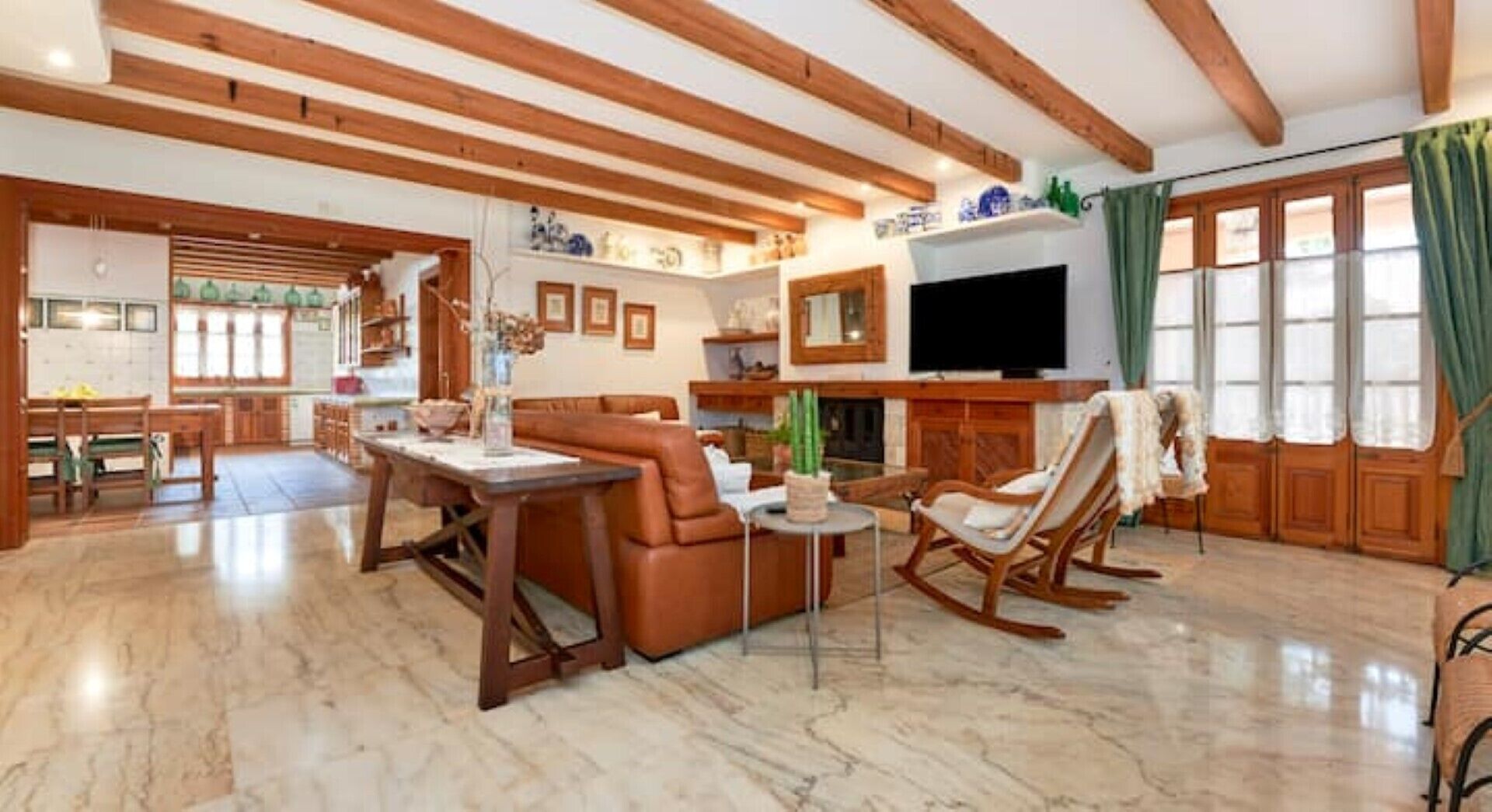 A spacious living room with a fireplace, a television, and a dining area with a kitchen in the background.